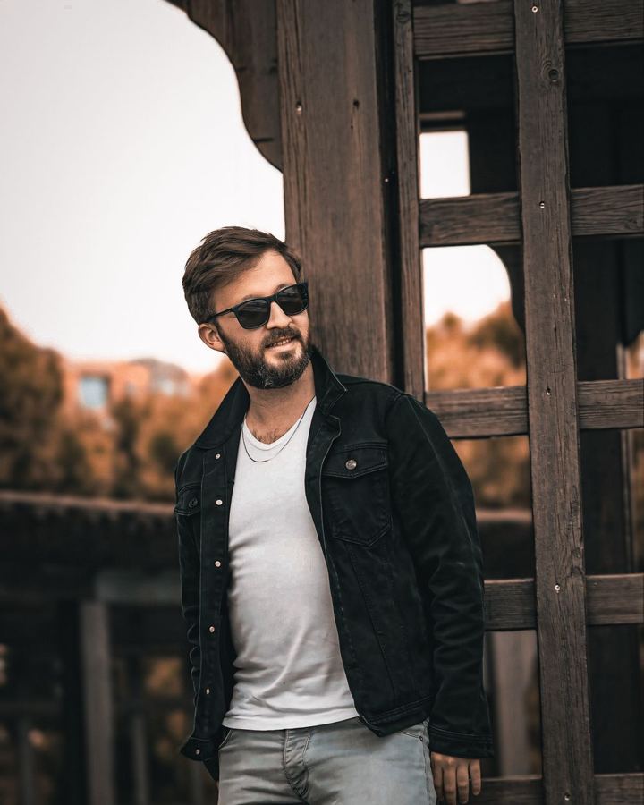 Man in a black jacket with grey trousers and sunglasses
